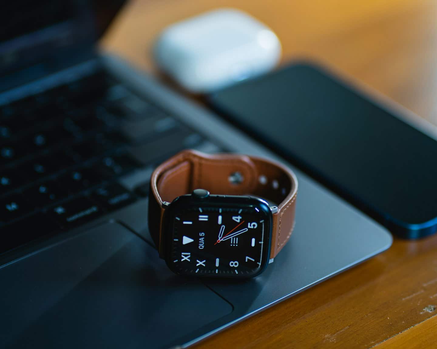 Uno smartwatch nero è appoggiato sulla tastiera di un laptop con smartphone e auricolari.
